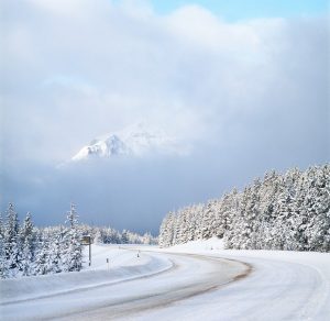 Photo shows a very snowy road, lined with trees, and snowcapped mountains in the distance, Canada's top ten weather stories 2017 by David Phillips