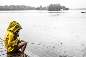 Photo shows a child in a yellow rain jacket with the hood up sitting at the side of a lake, Canada's top ten weather stories 2017 by David Phillips