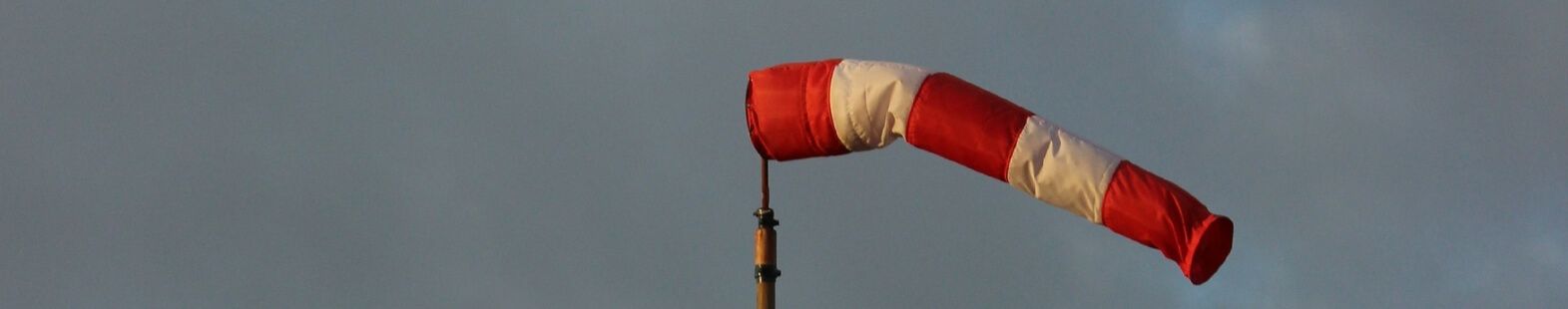 Image shows a red and white wind sock against a cloudy sky. Photo for the Wind at Lake Saint Charles article by Richard Leduc