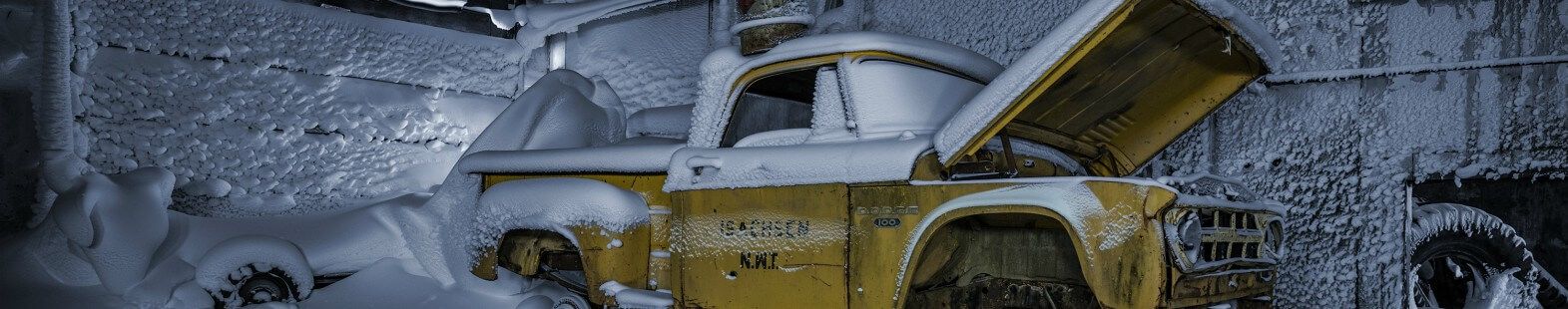 Image from Isachsen by aAron munson shows an old yellow pick up truck covered in snow, in a frozen garage