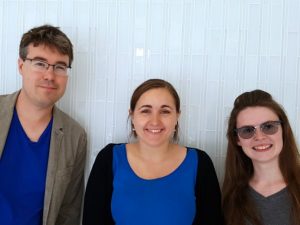 Photograph of three people. the authors of the article "watching the dust and clouds float lazily by during a martian summer." On left is a mad, late-thirties to early forties, white with glasses. Two other people are young women in their early twenties, both white with dark hair.