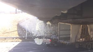 Image showing the moment of impact between a passenger vehicle and a transport truck, underneath a bridge.