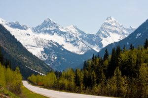 Highway through the Rogers Pass in the Canadian Rockies against a backdrop of forested hillsides and snow-capped mountain peaks.