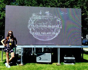 Samantha Mailhot is pictured standing beside a billboard sized projection of the carbon clock, on a sunny summer's day.