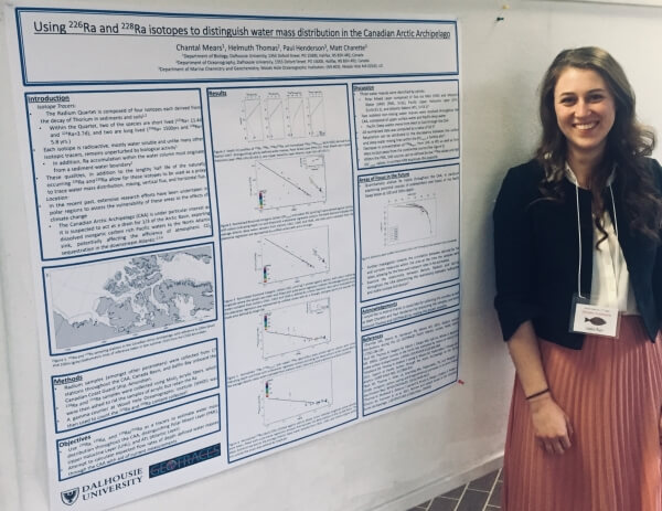 Photograph of a young woman, Chantal Mears, long brown hair, smiling, and standing beside a scientific poster.