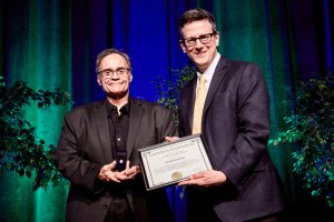 Photo of CMOS Fellow recipient in 2019 Richard Boudreault. Photo shows two smiling, middle aged, clean shaven caucasian men holding a certificate between them.