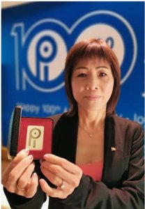 Photo of Xiolan Wang shows a gently beaming asian woman holding up a red velvet box with an award inside