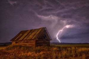 barn in empty field with lightning and dark purple sky