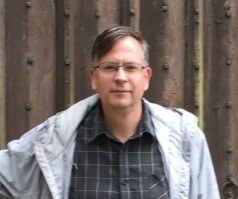 middle aged Caucasian man with parted brown hair and glasses outside smiling at camera