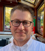 Smiling Caucasian man with thick rimmed glasses wearing earbuds