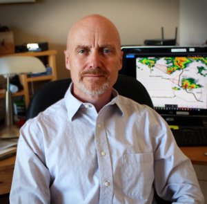 smiling bald Caucasian man with trimmed grey facial hair in pale button shirt