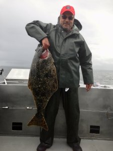 man in red hat and grey slicker holding up large caught fish by the gills