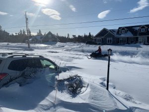 a photo taken of a snowstorm in St. John's Newfoundland featuring a car burried in snow and a person driving a snowmobile