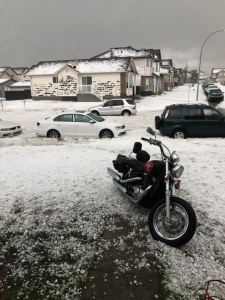 A photo of large hail on the ground taken from a driveway with a motorcycle on it