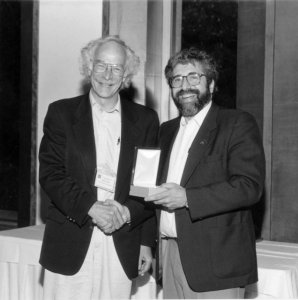 A black and white photo of a man receiveing an award from another man