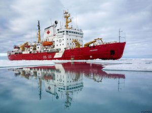 A red and white icebreaker with a perfect reflection on the water