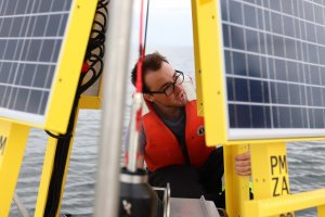 A person on a large buoy in the ocean with solar panels on it taking sampes