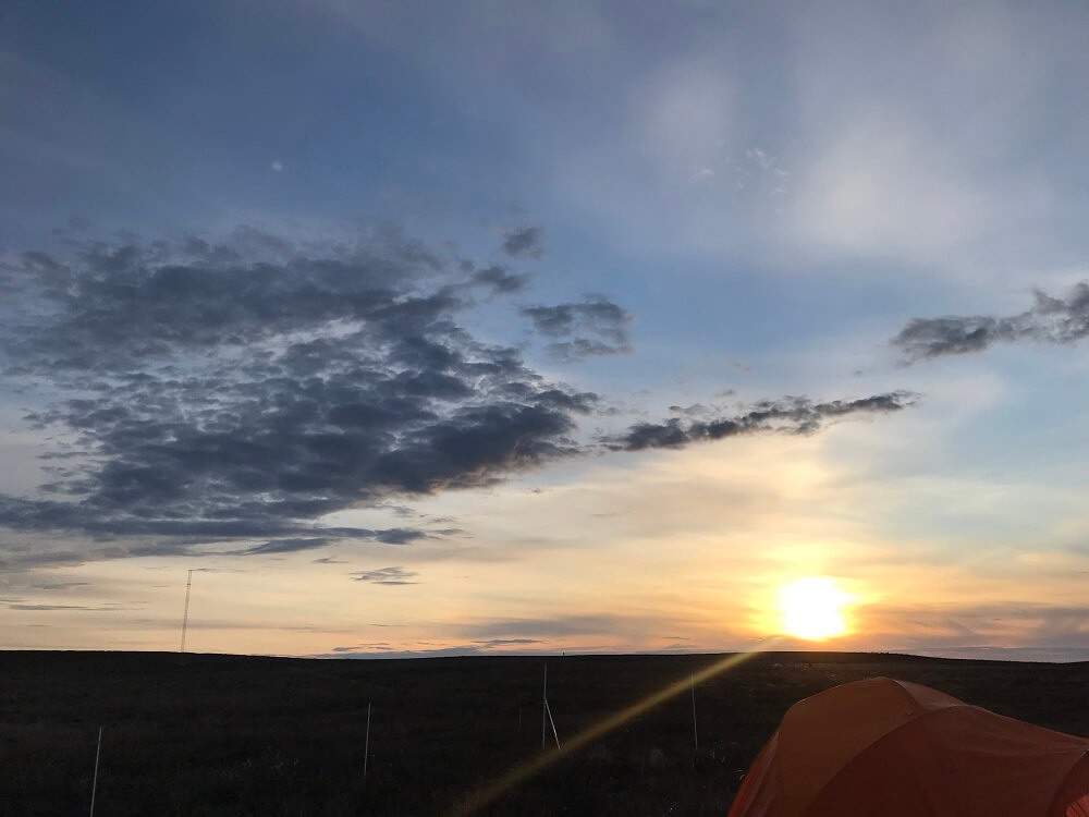 A sunset on the tundra with a few wispy clouds in the sky.