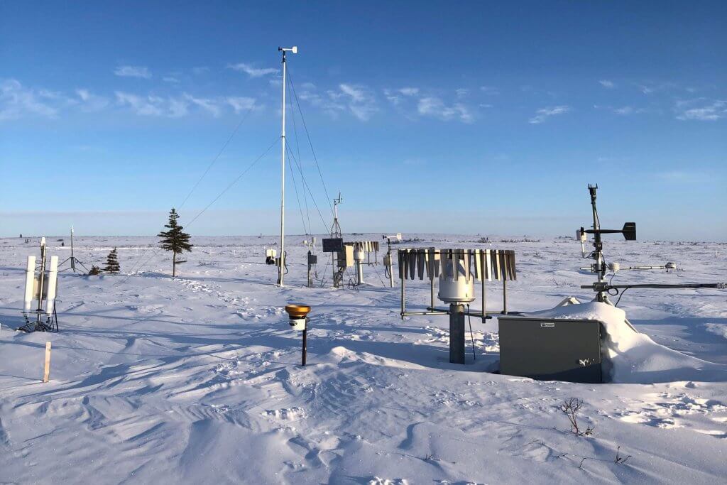 Paysage de toundra arctique par une journée de ciel bleu avec de nombreux instruments métalliques éparpillés dans le paysage.