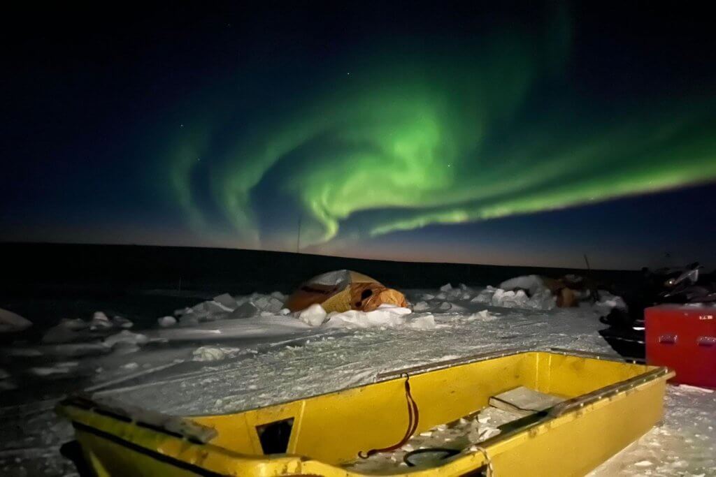 Photo de paysage d'aurores boréales avec un traîneau jaune et une tente orange au premier plan.